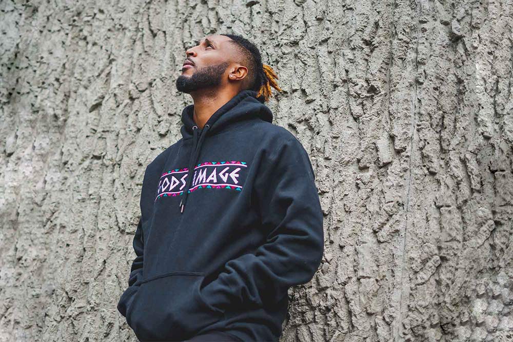 Man wearing a black hoodie with the words 'Gods Image'across the front of it. 
                    Man is looking up to the sky with his back against a stone wall.