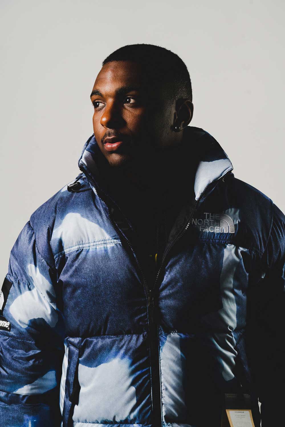 Man modeling
                blue camouflage North Face jacket. Man's torso facing camera while he looks to
                the left. Dark shadow across side of face.