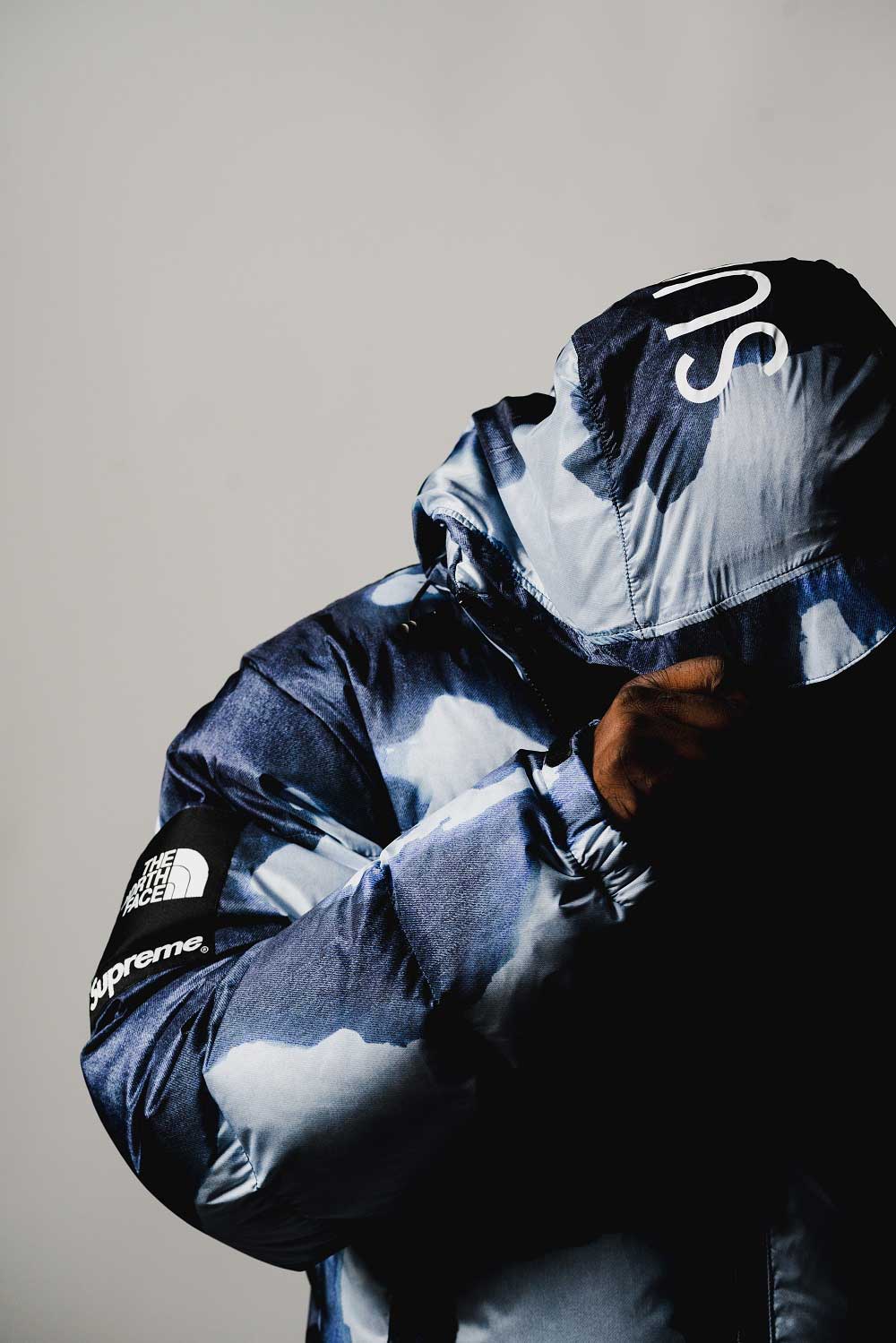 Man modeling
        blue camouflage North Face jacket. Man's face cannot be seen as he is holding 
        hoodie over his head.